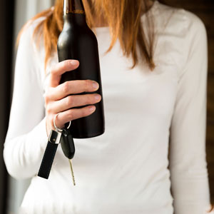 A woman holding a bottle of liquor and a car key in hand, potentially about to drive under the influence (DWI).